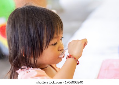 Soft Focus​ Of​ Happy Asian Baby Child Girl​eating Yogurt Food By Herself. Her Face Is Sloppy And Messy. 2-3​ Years​ Old​ Baby.​ Kid And Food Concept.