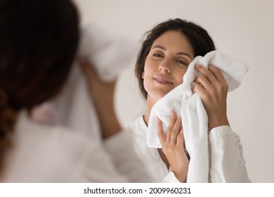 So soft. Happy young latin female wipe face with terry towel after morning shower enjoy delicate touch. Smiling millennial woman in white robe dry facial skin after washing with cotton bathroom linen