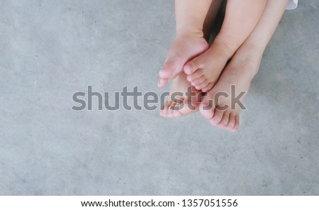 Soft image low section of Asian lovely mother's legs sitting and take a son to sit on her lap on cement floor at home, high angle view with copy space 