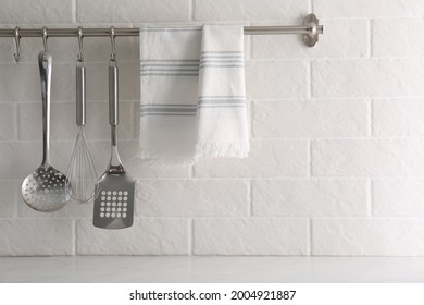 Soft Kitchen Towel And Utensils Hanging On Rack Near White Brick Wall