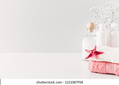 Soft Light Bathroom Decor For Advertising, Design, Cover, Set Of Cosmetic Bottles, Bath Accessories, White Small Flowers In Vase, Towel On White Wooden Shelf. Mock Up,copy Space
