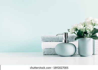 Soft light bathroom decor in mint color, towel, soap dispenser, white roses flowers, accessories on pastel mint background. Elegant decor bathroom interior