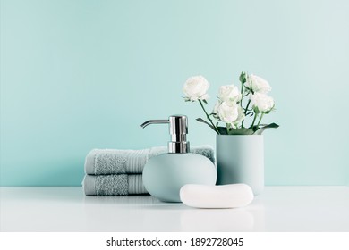 Soft light bathroom decor in mint color, towel, soap dispenser, white roses flowers, accessories on pastel mint background. Elegant decor bathroom interior