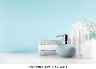 Soft Light Bathroom Decor In Pastel Blue Color, Towel, Soap Dispenser, White Flowers, Accessories On White Wood Shelf. Elegant Decor Bathroom Interior.