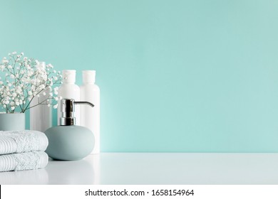Soft light bathroom decor in pastel blue color, towel, soap dispenser, white flowers, accessories on white wood shelf. Elegant decor bathroom interior.