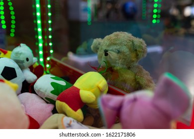 A soft lonely bear looks at the slot machine with soft toys with sadness.