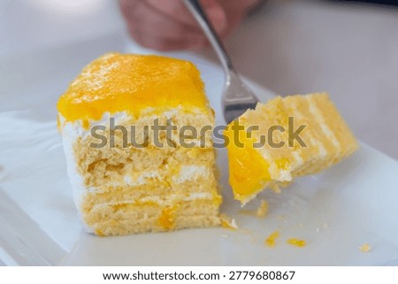 Soft mango cream cake slice with fluffy layers and fresh fruit topping served on a white plate with fork for sweet dessert enjoyment