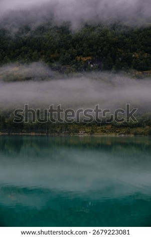 Soft mist blankets the pristine waters of Bergheimsvatnet, reflecting vibrant greenery. This peaceful setting embodies Norways natural beauty at dawn, inviting contemplation and exploration.