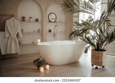 Soft native hues organic shapes look of bathroom with big window oval bathtub in neutrals tones. Green palm plants candles bubblebath leasure and relaxation skin selfcare wellness luxury living