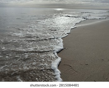 Soft ocean waves reaching a pristine sandy shoreline under a dramatic cloud-filled sky. A tranquil seascape capturing the beauty of Australia’s peaceful coastline.