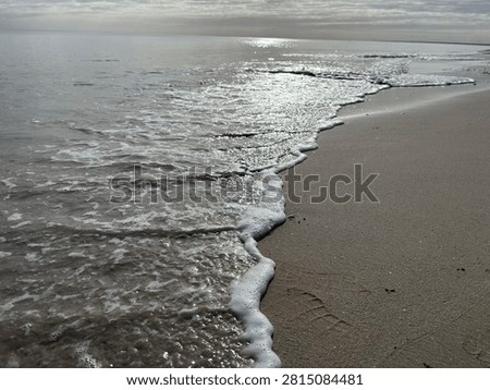 Soft ocean waves reaching a pristine sandy shoreline under a dramatic cloud-filled sky. A tranquil seascape capturing the beauty of Australia’s peaceful coastline.