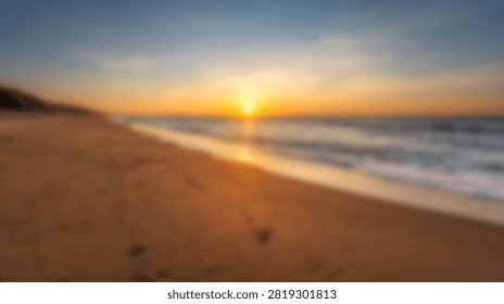 A soft out of focus view of a sandy beach shoreline during a vibrant golden sunrise or sunset