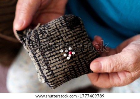 Soft pad for sewing needles. Elderly hands of a seamstress hold a tool. View from above.