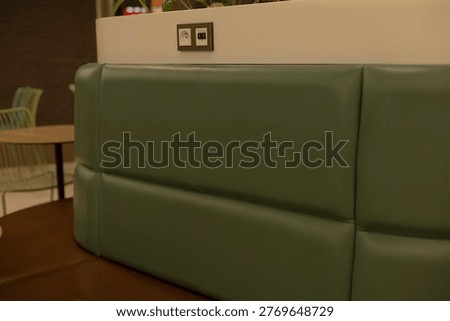 Soft panel seating hugging planter edge with outlet, muted green upholstery, subtle mall signage in distance, interior objects emphasize modern communal furniture and calm