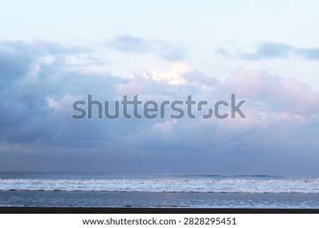 Soft pastel clouds drift above the calm ocean. Wavelets roll gently toward the shore, untouched by wind. Distant horizon blends sky and sea in muted tones
