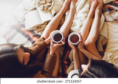 Soft photo of two  sisters  on the bed with old books and cup of tea in hands wearing cozy sweater , top view point. Two best friends enjoying morning.