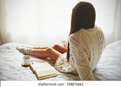 Soft Photo Of Woman On The Bed With Old Book, A Cup Of Coffee And Smart Phone