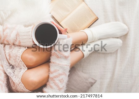 Soft photo of woman on the bed with old book and cup of coffee in hands, top view point