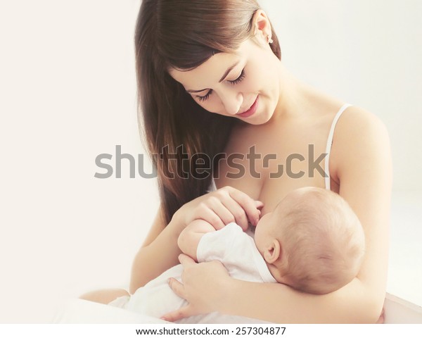 白い部屋の家で赤ん坊に乳を飲ませる柔らかい写真の若い母親 の写真素材 今すぐ編集