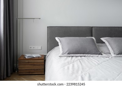 soft pillows and cotton blanket on bed with grey headboard, open book on wooden side table and metal lamp in room with modern interior