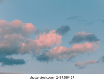 Soft, pink clouds float in a blue sky during sunset, creating a peaceful and picturesque evening scene.