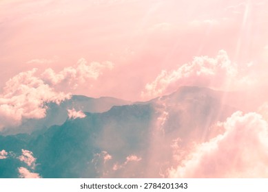 Soft pink clouds gently enveloping rugged mountain peaks create a breathtaking sunset panorama, evoking tranquility and awe in the serene evening atmosphere