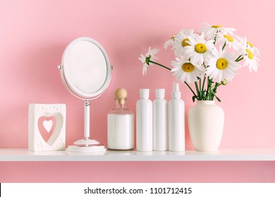 Soft Pink Light Bathroom Decor For Advertising, Design, Cover. Cosmetic Set On Light Dressing Table. Beautiful Flowers In A Vase On A Pink Wall Background, Mirror On A Wooden Shelf. Mock Up