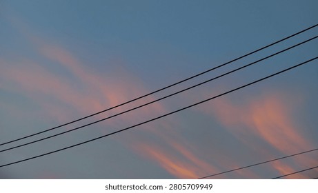 Soft pink sunset clouds stretch across a blue evening sky, crossed by power lines, creating a peaceful urban atmosphere with pastel colors and minimalist composition.