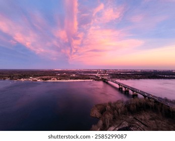 Soft pink sunset reflecting in the Dnipro river. Pink evening river with long bridge in the evening