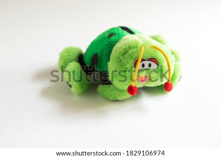 Soft plush toy for children - green ladybug. A beetle with sad eyes, red bells on its antennae, unrealistic color with black spots and large paws.Children's toy close-up, space for text