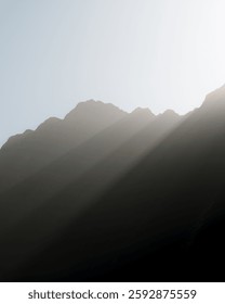 Soft rays of sunlight filter through the mountains at Milford Sound, creating a serene atmosphere as shadows dance over the landscape during early morning.