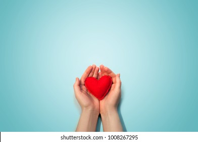 Soft Red Toy Heart in the Woman Hands on Light Blue Background. Valentine Day Concept. Flat Lay Top View. Copy Space For Your Text.