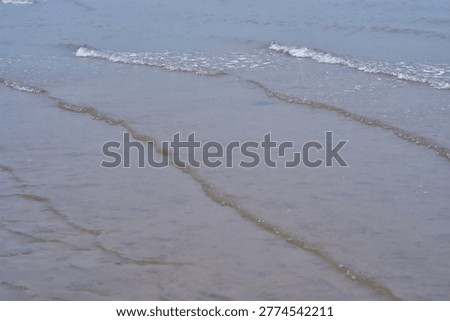 Soft rolling waves creating repetitive patterns on shallow shoreline water.