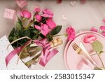 A soft and romantic dinner setup featuring pink plates, golden cutlery, a champagne glass, fresh roses, and heart decorations.