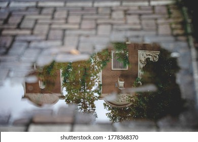 Soft selective focus of puddle on the street with reflection on water, Shadow of architecture features traditional houses along canal, Summer cityscape in raining day, Amsterdam, Netherlands.