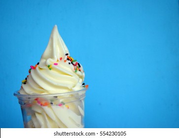 Soft Serve Ice Cream In A Plastic Cup With Sprinkles Topping On Bright Blue Background With Copy Space