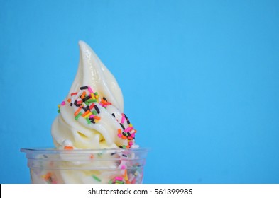 Soft Serve Ice Cream In A Plastic Cup With Sprinkles Topping On Bright Blue Background With Copy Space