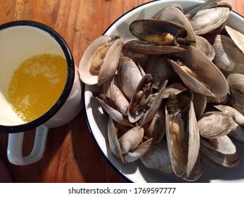 Soft shell steamer clams with drawn melted butter in white enamelware on wooden table