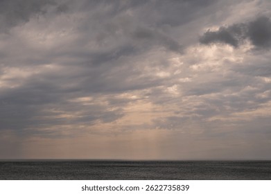 Soft sun rays breaking through cloudy sky over calm sea horizon. Atmospheric seascape with light beams, dramatic clouds and peaceful mood, ideal for nature, weather and abstract background use