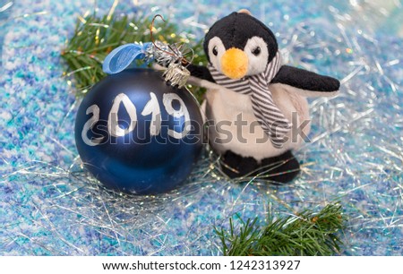 The  soft toy in a form of a penguin on a silver tinsel with Christmas ball with figure 2019. New year/Christmas background