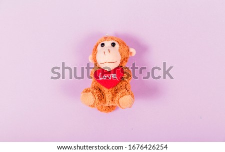 Soft toy monkey holding a heart in his hands on a purple background