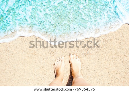 Soft wave of blue ocean on sandy beach Background with women feets, view from above. Tropical summer vacation concept.
