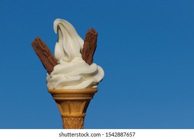 Soft whipped vanilla ice cream in a cone with two chocolate flakes against a blue sky. Often known as a 'double flake 99'. The image has space for copy