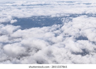 Soft white clouds blanket the sky, revealing a faint glimpse of land below through scattered openings. Scene captures the serene beauty of an aerial view above dense cloud layers