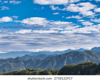 Soft white clouds drift over a serene mountain range during a clear day, evoking a profound sense of tranquility and the vastness of the natural world.