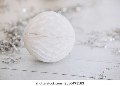 A soft white paper ornament rests on a wooden surface, accented by scattered silver tinsel. This charming decoration captures the essence of Christmas and New Year celebrations. - Powered by Shutterstock