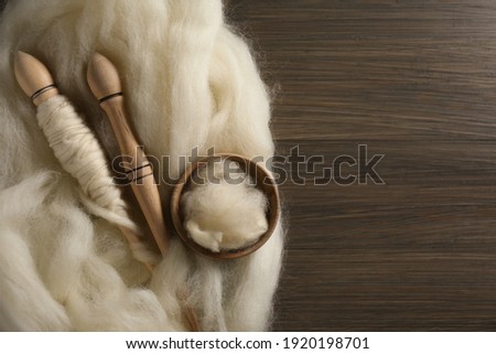 Soft white wool and spindles on wooden table, flat lay. Space for text