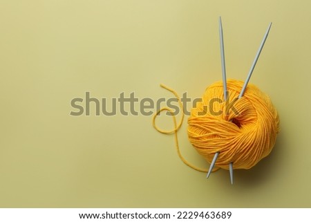 Soft woolen yarn and knitting needles on yellow background, top view. Space for text