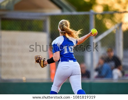 Softball pitcher throwing to first base and player sliding into base safely