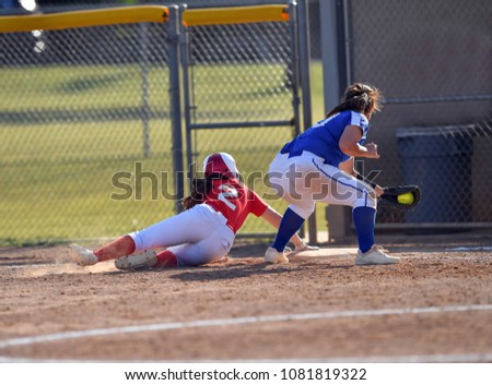 Softball pitcher throwing to first base and player sliding into base safely